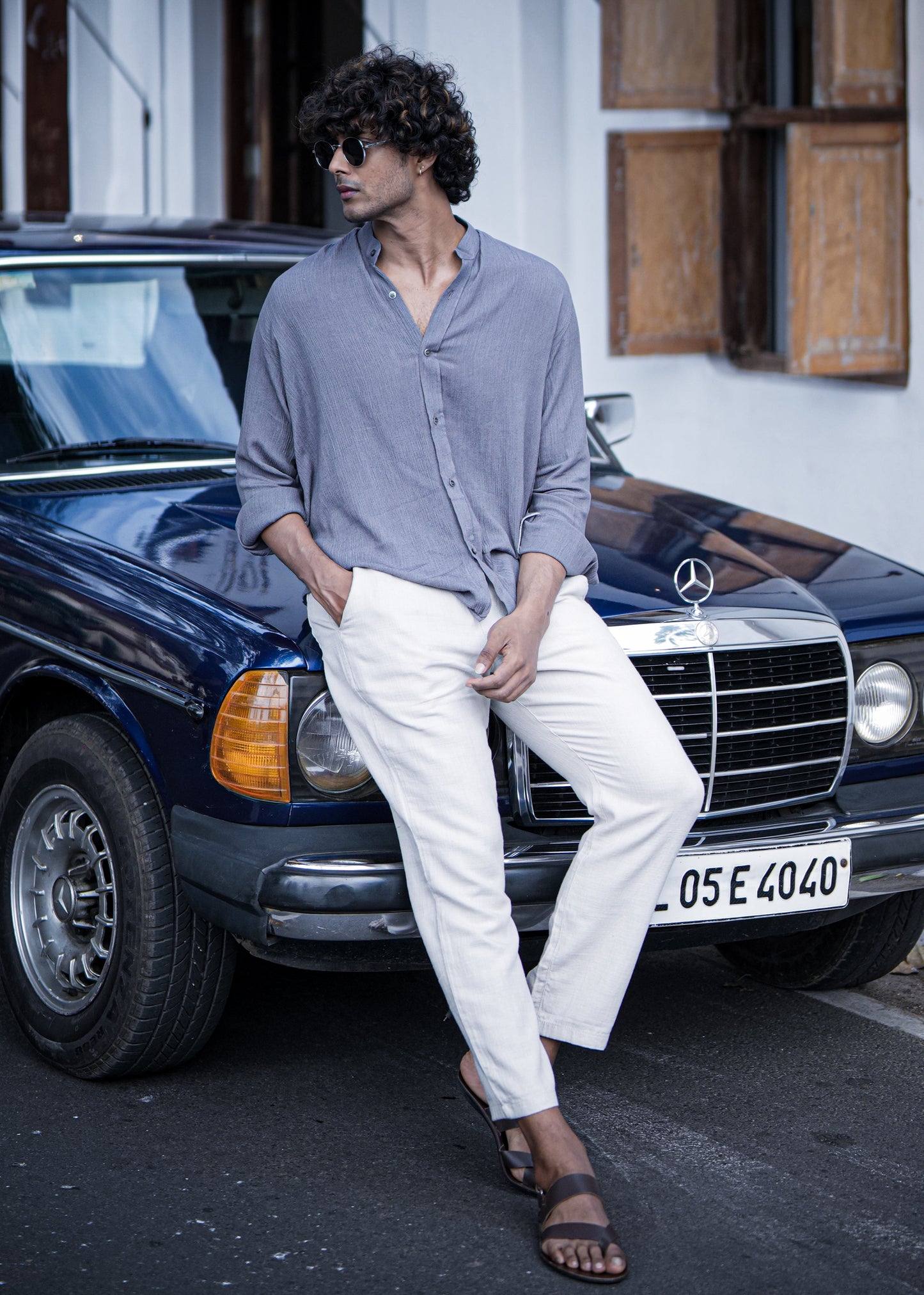 "Mod Maven Lilac Grey Crushed Cotton Full Sleeve Shirt paired with Off-White Comfortable Fit Pants. Model sitting on a vintage dark blue car, wearing shades, showcasing a chic street style look."