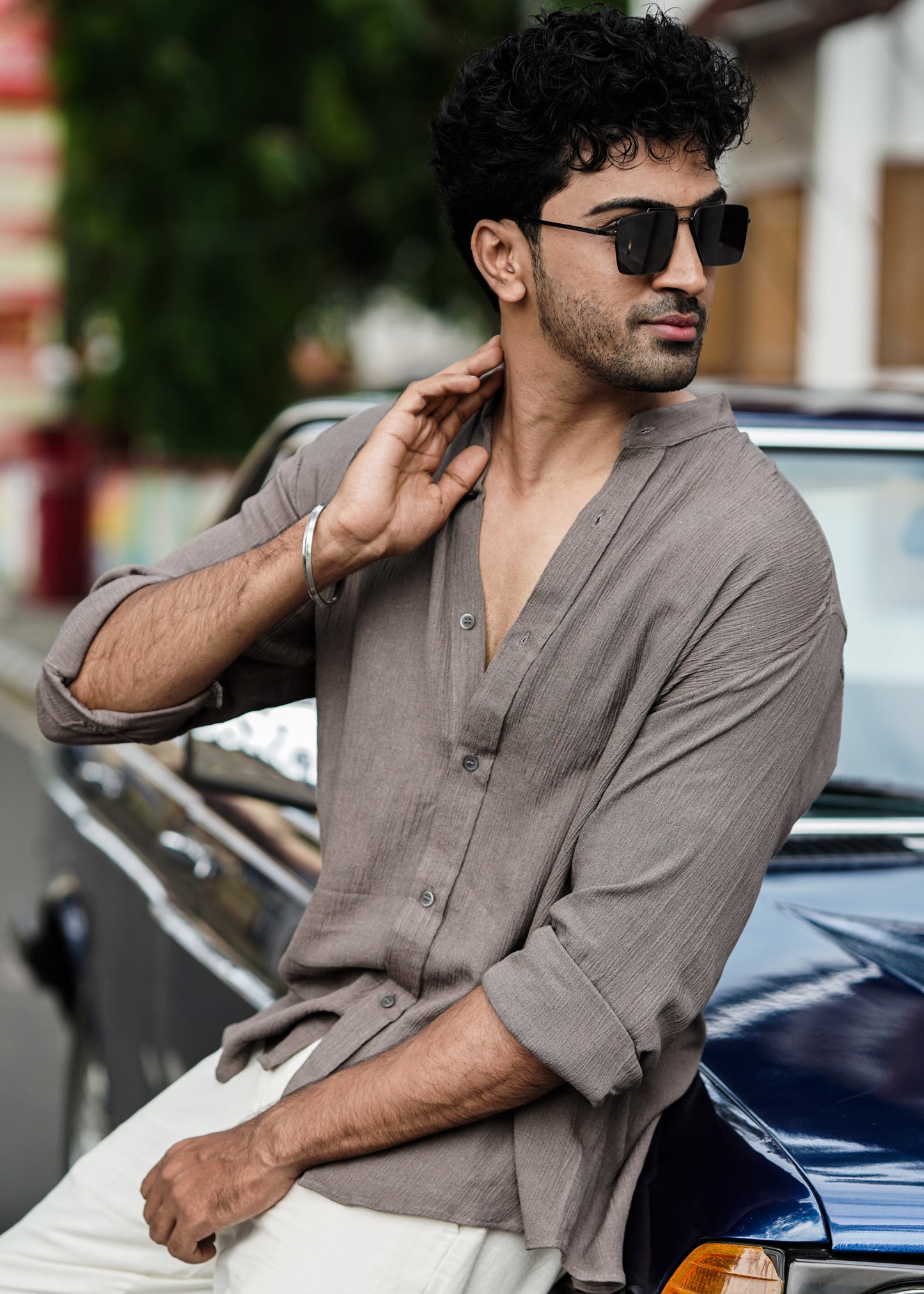 "Mod Maven Nude Brown Crushed Cotton Full Sleeve Shirt paired with Off-White Comfortable Fit Pants. Model leaning on a vintage dark blue car, looking to his left wearing shades, showcasing a chic street style look."