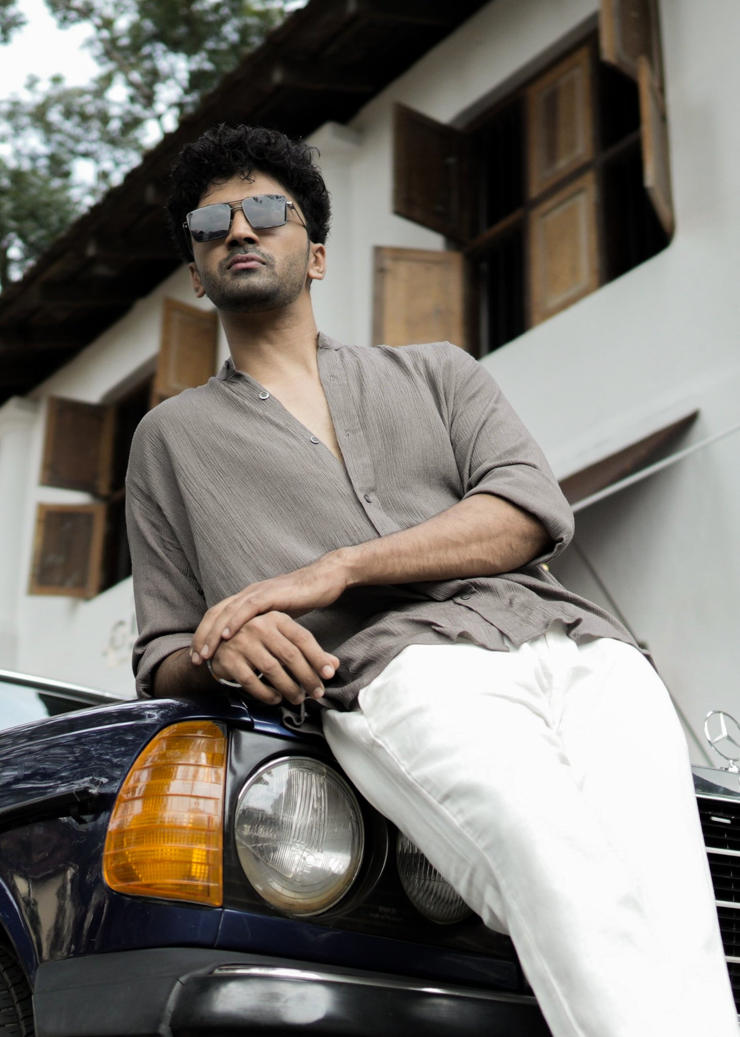 "Mod Maven Nude Brown Crushed Cotton Full Sleeve Shirt paired with Off-White Comfortable Fit Pants. Model leaning on a vintage dark blue car, wearing shades, showcasing a chic street style look."