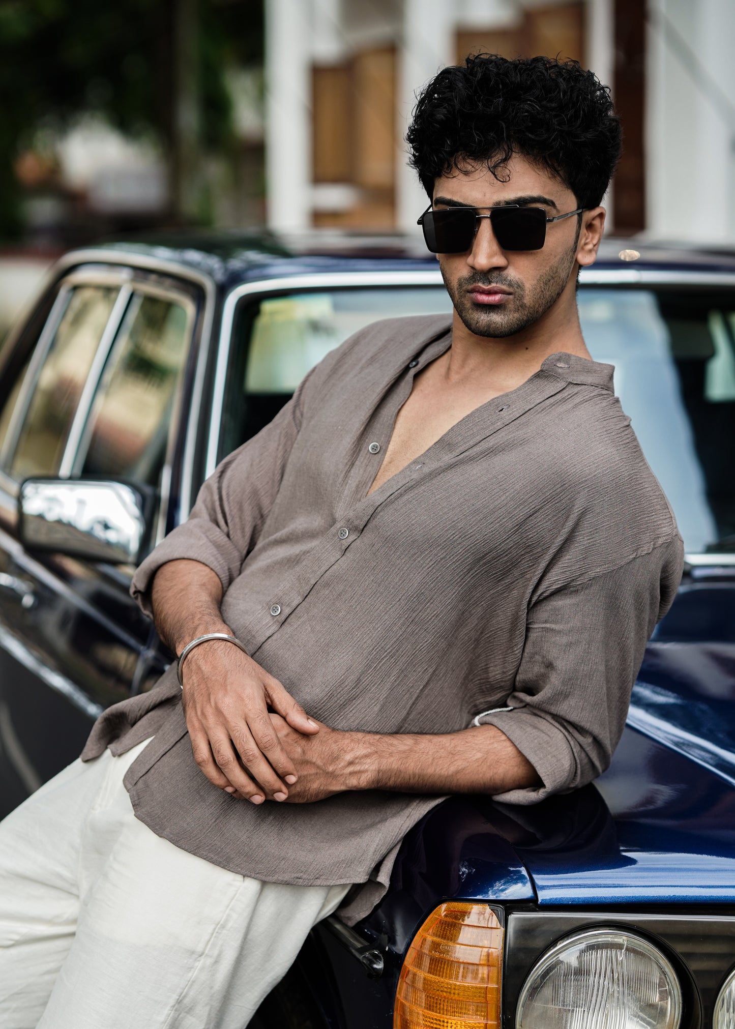 "Mod Maven Nude Brown Crushed Cotton Full Sleeve Shirt paired with Off-White Comfortable Fit Pants. Model leaning on a vintage dark blue car, wearing shades, showcasing a chic street style look."