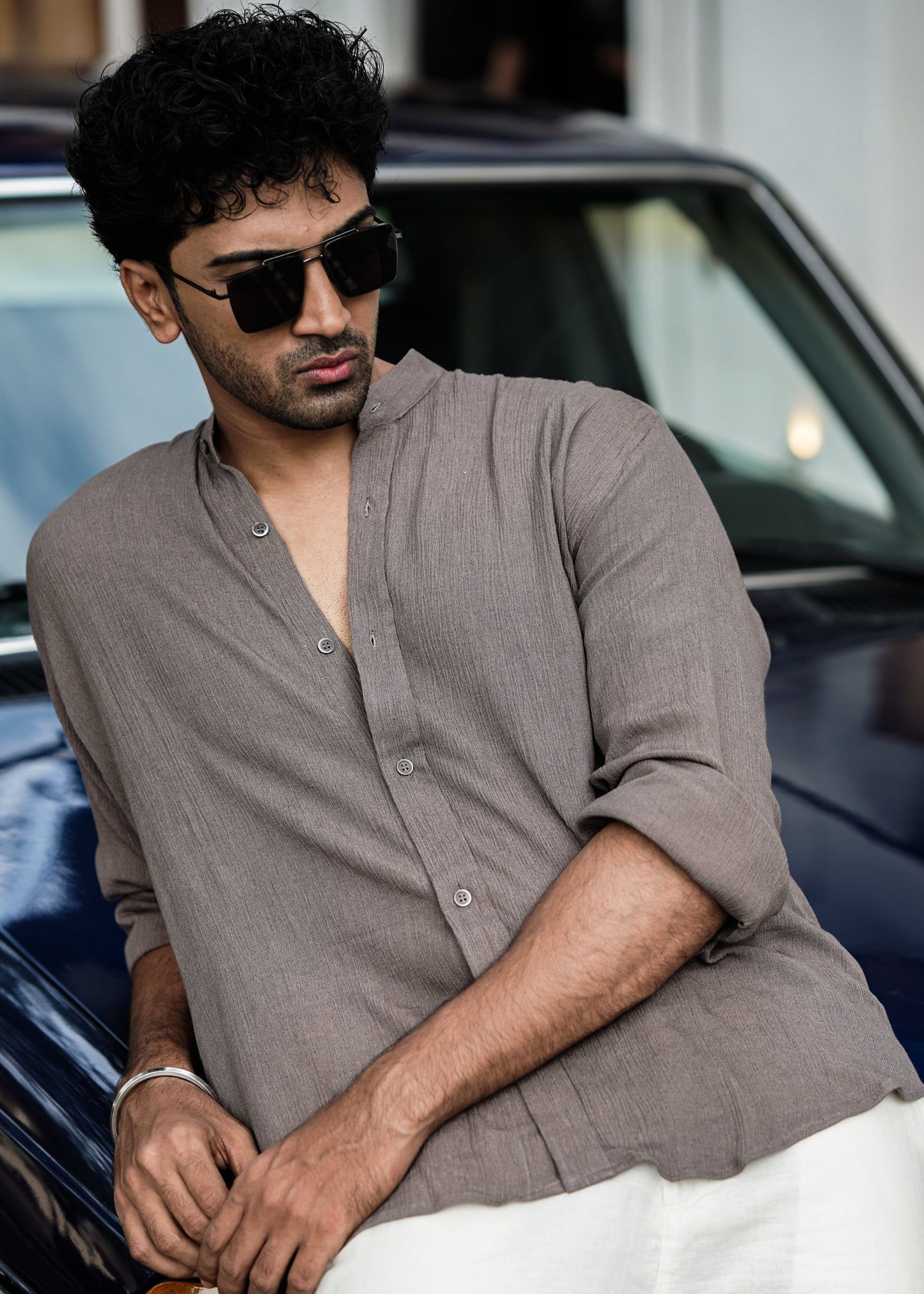 "Mod Maven Nude Brown Crushed Cotton Full Sleeve Shirt paired with Off-White Comfortable Fit Pants. Model leaning on a vintage dark blue car, face down, wearing shades, showcasing a chic street style look."