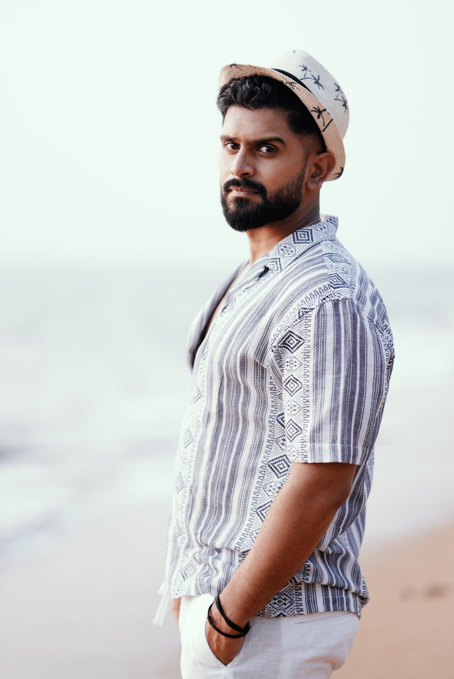 Aside profile view of a model wearing a geometric weave patterned shirt with relaxed short sleeves and a lightweight design. The subtle texture of the fabric adds depth to the nomadic-inspired style.