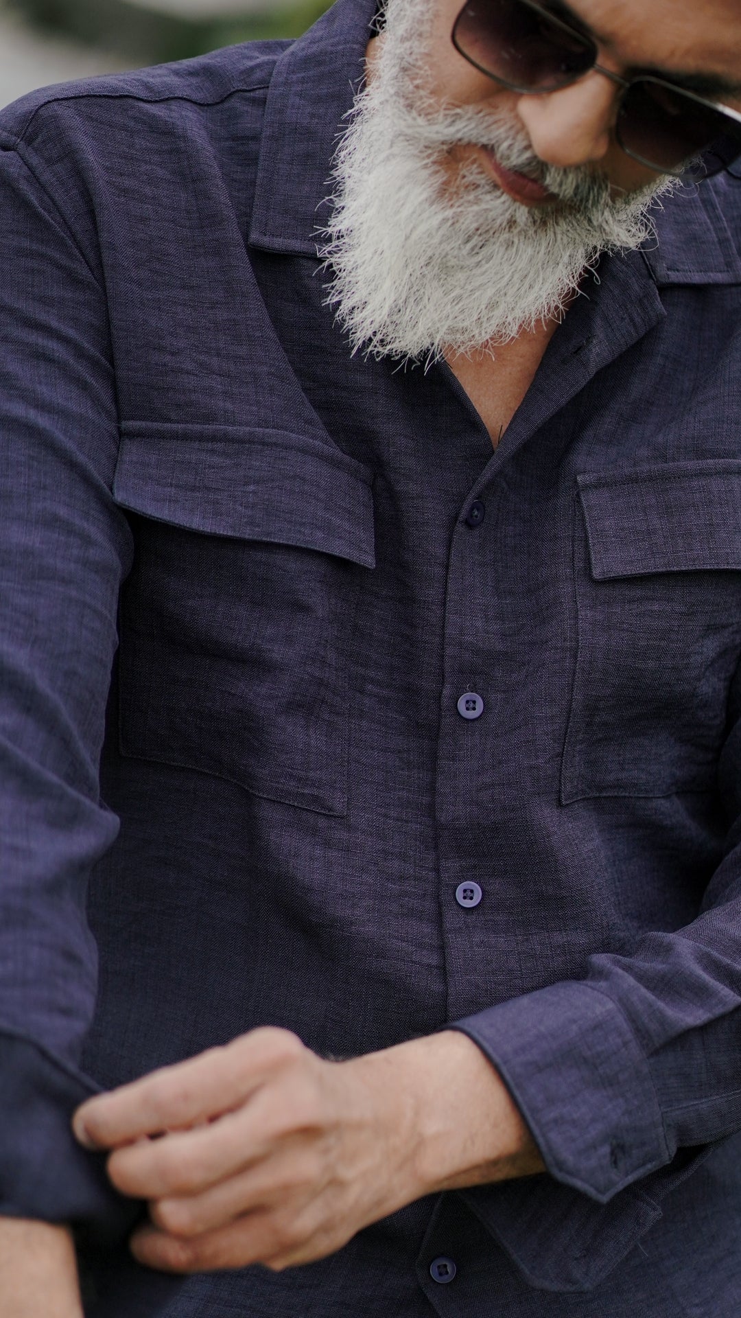 A distinguished older male model with a gray beard and stylishly combed gray hair is wearing an navy blue, double-pocket, full-sleeve shirt from Mod Maven, standing confidently against a textured, natural background. The picture focuses on the collar and pocket detail